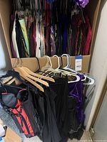 Photo of assorted ladies dresses and blouses hanging in closet on hangers, mostly dark colored and patterned fabrics.