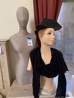 Mannequin form shown beside another mannequin torso with a head and dressed in a black cropped jacket and mortarboard hat, demonstrating relative size and condition.