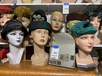 Seven mannequin heads on shelf wearing assorted hats and small arched mirror on tabletop