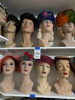 Eight mannequin heads displayed on white shelves wearing various hats.