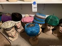 Row of mannequin heads on floor shelf wearing assorted vintage hats
