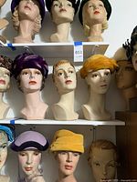 Three mannequin heads on top shelf wearing purple, black, and green hats