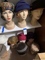 Three mannequin heads on a shelf wearing feather-print, blue knit and black beret hats.