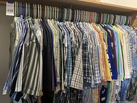 Wide view of multiple men's shirts hanging on a rack with mixed patterns mostly in pastel and muted color tones, sizes XL to 3XL.