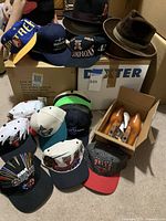 Group of two dress hats and seven baseball caps arranged on a box and on the floor