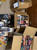 Three cardboard boxes of assorted VHS tapes on carpet