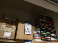 Photo showing two cardboard boxes labeled with 495 CDs taped closed and a tall stack of CD cases on a shelf
