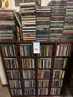 Photo of a dark wooden CD holder filled with rows of compact discs and additional stacks of CDs on top and beside it.