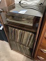 Full view of wooden cabinet with record player on top shelf and two shelves of records below