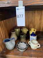 Photo showing 8 pottery pieces including vases, pitchers, bowl, and lidded jar on a wooden shelf.