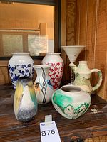 Photo showing six pottery vases of various shapes, sizes and glazes on wooden surface near window.