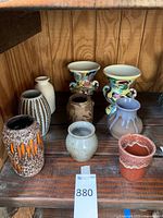 Photo showing nine pottery vases on wooden surface with various finishes and shapes