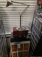 Desk lamp on red General Electric radio and black Sony CD player atop white storage stand filled with vinyl records
