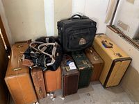 Overview of seven suitcases and two travel bags in a corner, showing variety in size, color, and material.
