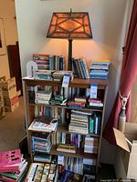 Full view of wooden bookcase filled with books and tabletop lamp on top