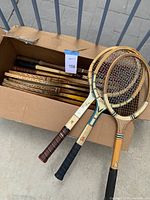 Photo showing a box with multiple wooden tennis rackets, focusing on the handles and frames inside the box.