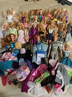 Overall view showing approximately 22 vintage Barbie dolls dressed in a variety of outfits, with loose accessories scattered in front