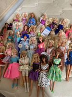 Overall view of about 34 vintage Barbie dolls in various outfits and hair styles laid on a mattress.