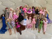 Overview photo showing 25 vintage Barbie dolls in various outfits and hairstyles, laid out on a bed mattress.