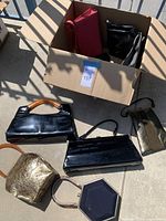 Top-down view of six vintage purses and bags placed on concrete floor and in an open box.