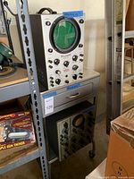 Full view of oscilloscope on metal cart shelf with drawer visible.