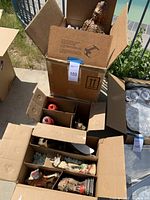 View of multiple open boxes showing various vintage statues including a Native American figure, blue lion, ship, red-topped figurines, and other smaller statues packed with packing peanuts and cardboard dividers.