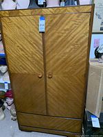 Full front view of the wooden wardrobe showing two doors with angled wood grain pattern and round wooden handles.
