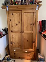 Front view of the wooden wardrobe dresser showing two paneled doors and single bottom drawer, with round wooden knobs, light wood with knots.