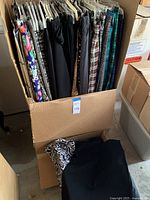 Multiple women's ski skirts size small on hangers in a cardboard box with some folded skirts below.