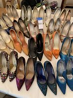 Photo showing a large variety of women's stiletto high heel shoes arranged on a table, various colors and designs visible, some vintage style evident.