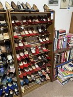 Wooden shoe rack filled with various pairs of women's shoes, including red, blue, and patterned styles, placed next to a pile of books.