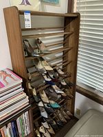 Full view of wooden shoe rack with shoes displayed on multiple horizontal slats, positioned near a window and stacked books.