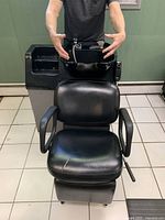 Front view of black shampoo chair with armrests positioned in front of black porcelain basin