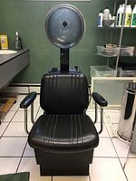 Front view showing black salon chair with attached large round hair drying hood above.