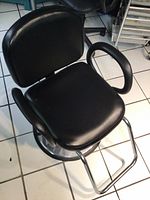 Front and top view of black vinyl salon chair showing padded seat and armrests on round chrome base with footrest.