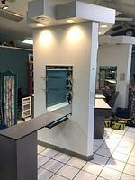 Wall-mounted manicure station showing glass shelving, smaller mirror, wrist rest, and storage drawers against a wall with lighting above.