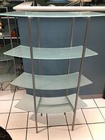 Front view of frosted curved glass shelf with four tiers and silver metal frame.
