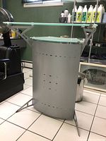 Side view of frosted glass and silver metal bar table showing the curved perforated metal panel and glass shelves.