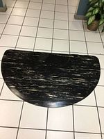 Top down view of the large black floor mat with white streaks, half circle shape placed on white tiled floor