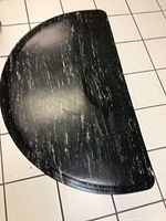 Black and white streaked half circle rubber floor mat laid on white tiled floor, showing texture and pattern from top view