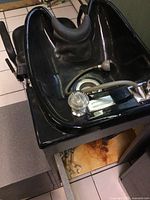 Close-up of the black plastic shampoo bowl with faucet, spray nozzle, and cushioned neck rest