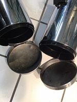 View inside the open trash cans showing cylindrical shape and black plastic inner lids.