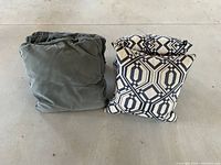 Four decorative pillows laid out on the floor: two blue velvet pillows folded or stacked on the left, two blue and beige geometric patterned pillows stacked on the right.