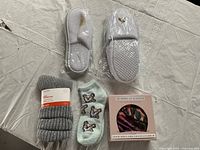 Two pairs of hotel slippers in plastic wrapping along with two pairs of socks on a white sheet.
