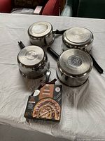 Four silver pans shown upside down, bottom branding visible, and a boxed cinnamon bun recipe on white cloth.