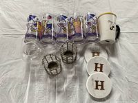Top-down view of all five retro plastic glasses, honey bee mug, three marble coasters with 'H' monogram, and three glass tea light holders arranged on a white textile surface