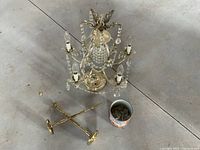 Top view of crystal chandelier, brass lamp components, drapery hooks, and decorative container on floor.