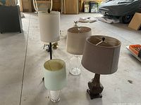 Four lamps with different bases including glass, pottery pineapple, and metal bases with neutral-colored shades