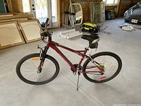Side view of burgundy mountain bike showing full frame, tires, pedals, and handlebars in a garage setting.