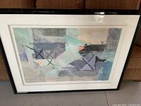 Framed abstract print with visible artwork details, black frame, and white matte. Displayed sitting against a brown upholstery background.